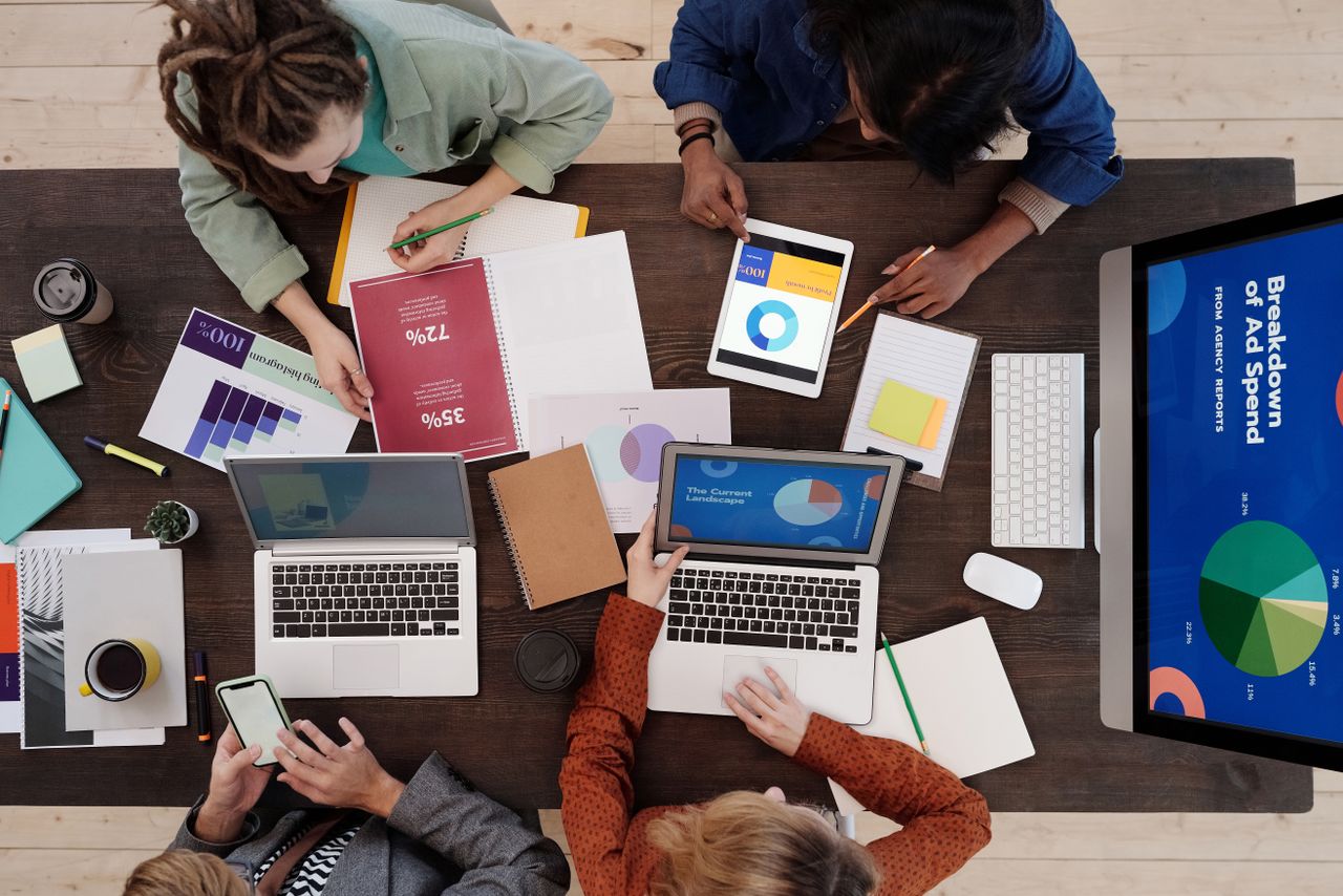 Un equipo diverso colabora en una mesa en estrategias de marketing digital, usando portátiles y tabletas.